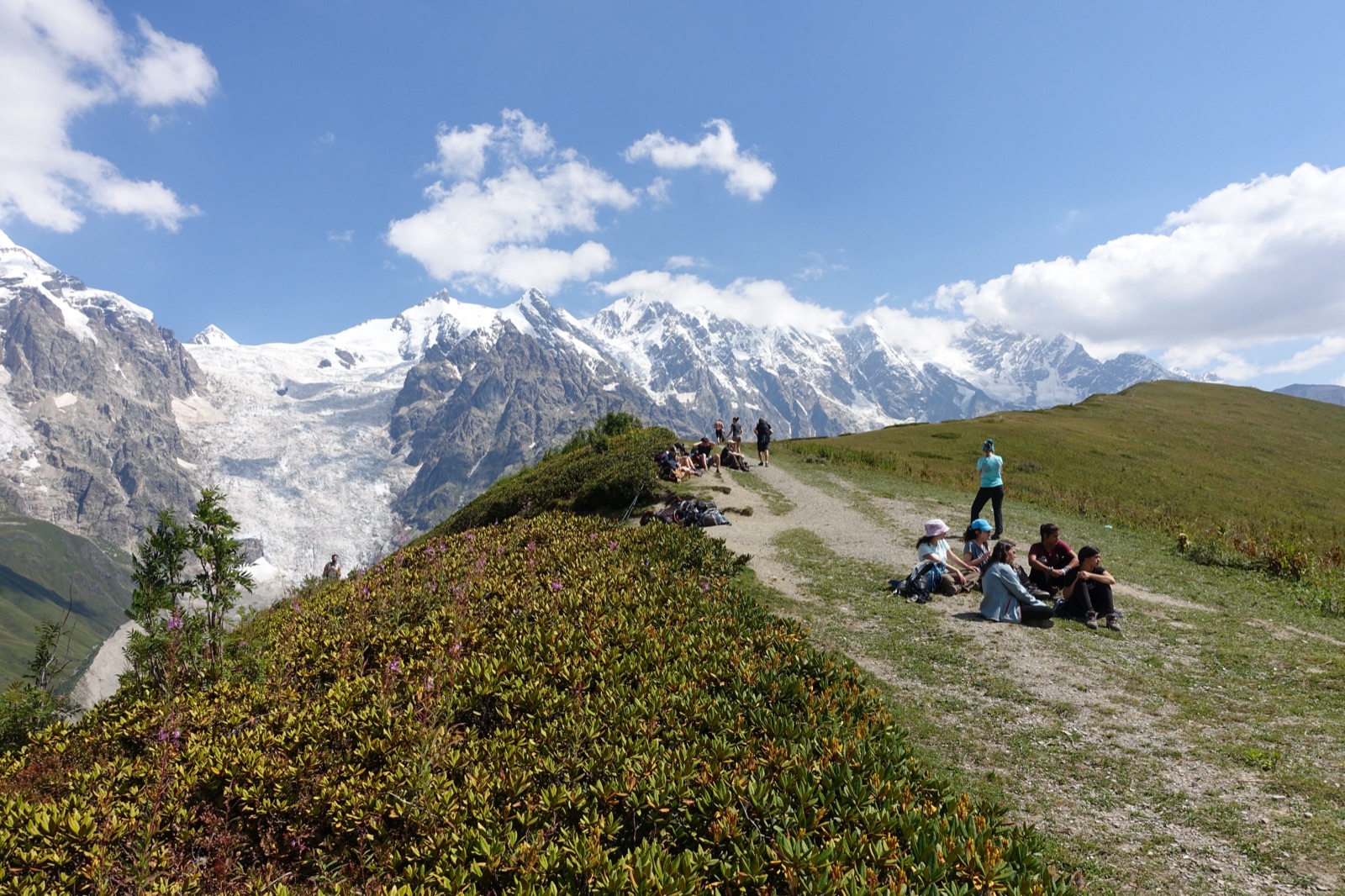 Hikers resting beside the Mestia-Ushguli trail with the Adishi Glacier behind them